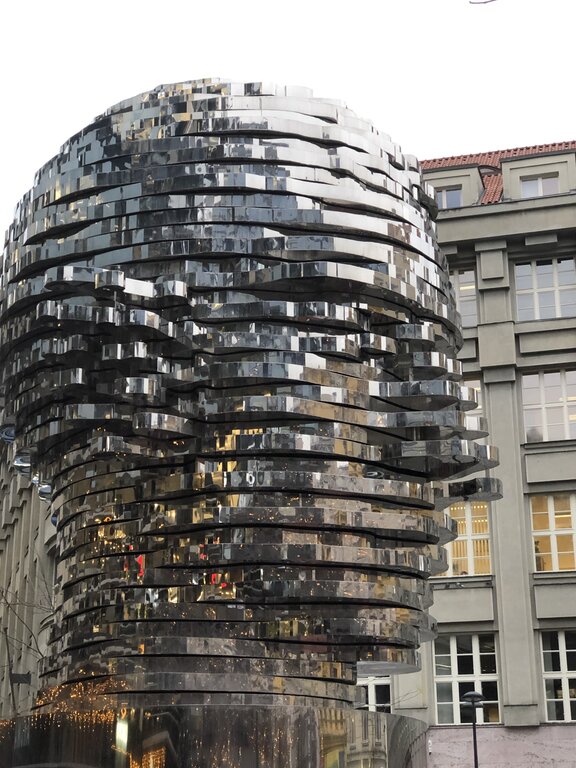 A striking kinetic sculpture of Franz Kafka’s head in Prague, made of stacked, reflective metal plates that rotate independently. Created by artist David Černý, the sculpture gives the illusion of constant transformation as the layers shift. The mirrored surface reflects the surrounding buildings, blending the artwork with the urban landscape.