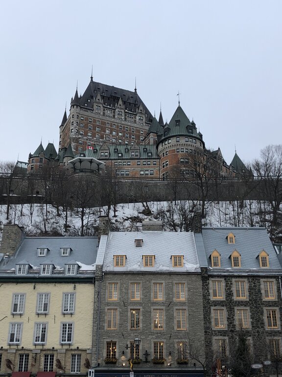 Château Frontenac rises majestically behind a row of colorful 18th-century buildings, all dusted with snow. This iconic view represents the heart of Quebec in winter.