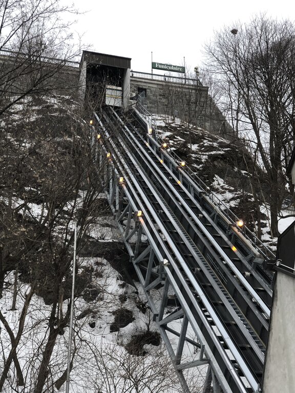 The Funiculaire du Vieux-Québec climbs a steep snowy hillside through a metal track flanked by bare winter trees. This historic funicular connects Lower and Upper Town in Quebec in winter.