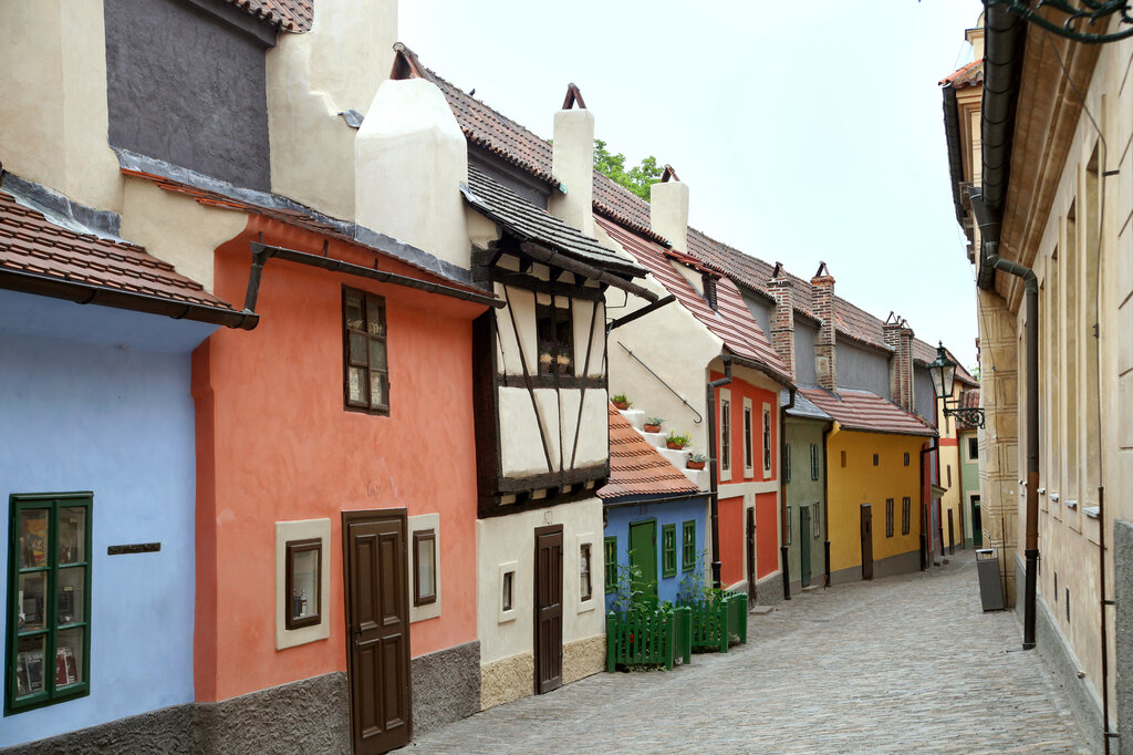 Golden Lane in Prague Castle features a narrow cobblestone street lined with charming, colorful houses with red-tiled roofs and small doors.