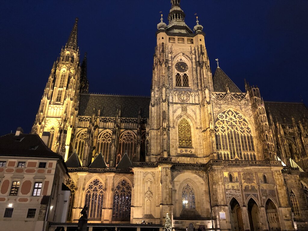 St. Vitus Cathedral in Prague Castle is illuminated at night, showcasing its Gothic arches, tall spires, and intricate stained-glass windows.