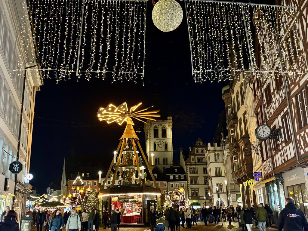 The illuminated wooden Christmas pyramid stands tall at the center of the Trier Christmas market, surrounded by festive lights and half-timbered buildings.