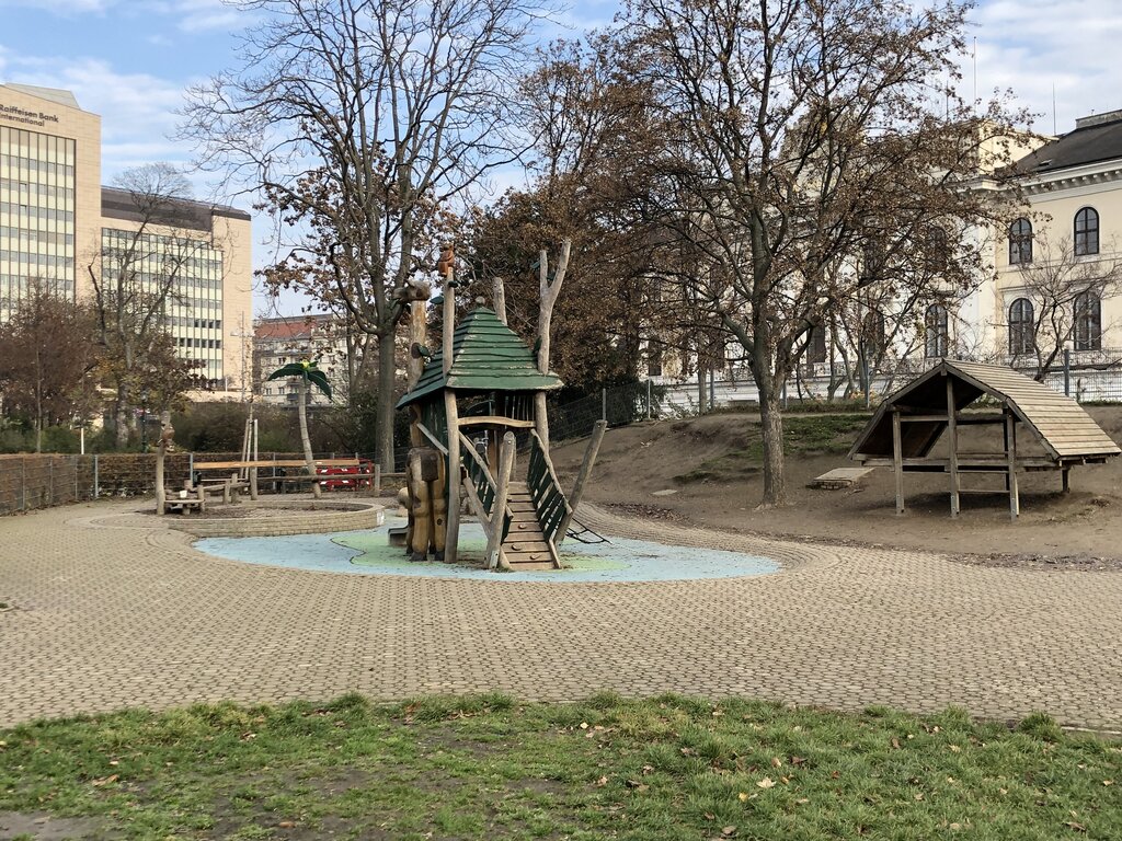 A toddler sized wooden play structure resembling a treehouse stands in the middle of the Stadtpark playground in Vienna, surrounded by leafless trees and quiet paths on a winter day.