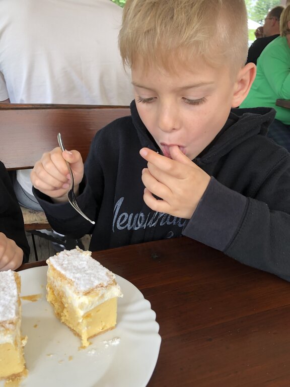 Child eating a slice of Bled cream cake dusted with powdered sugar at an outdoor cafe in Ljubljana. The creamy custard layers are visible between the flaky pastry.