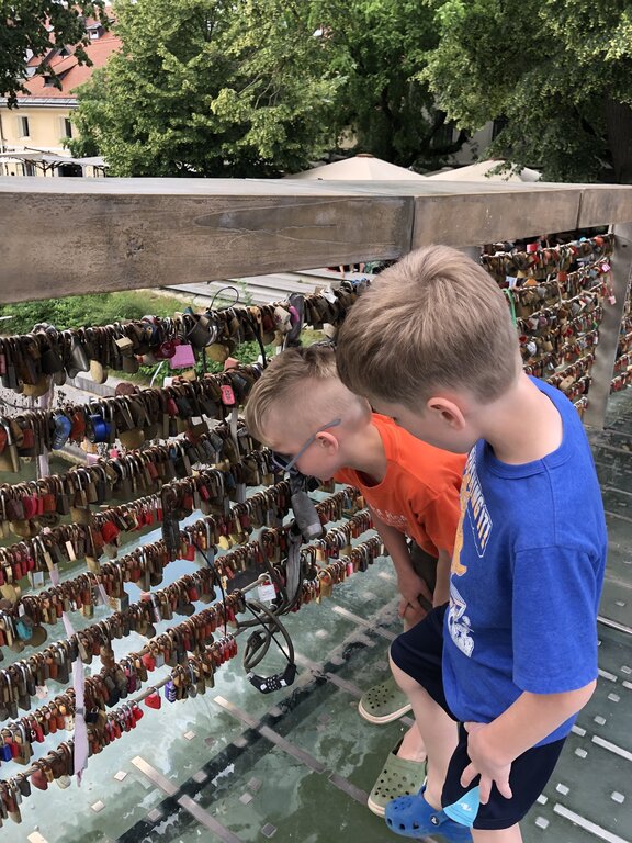 Two children looking over a bridge railing covered in love locks above the Ljubljanica River. Hundreds of small padlocks in different colours are attached to the metal bars.