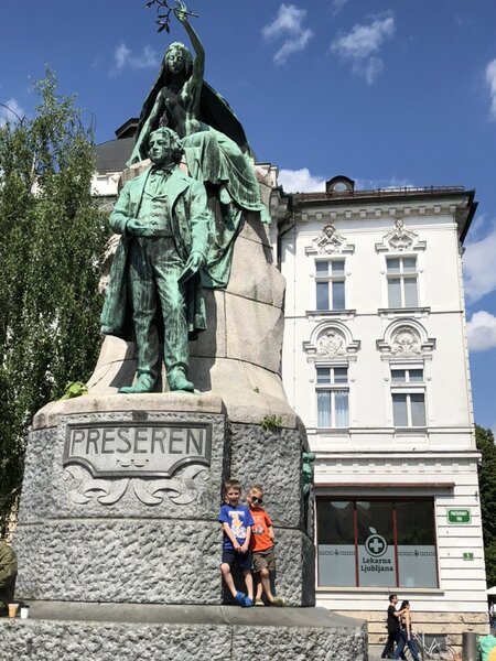 Statue of France Prešeren standing on a large stone pedestal engraved with Preseren while two children lean against the base in Prešeren Square in Ljubljana Slovenia on a sunny day.