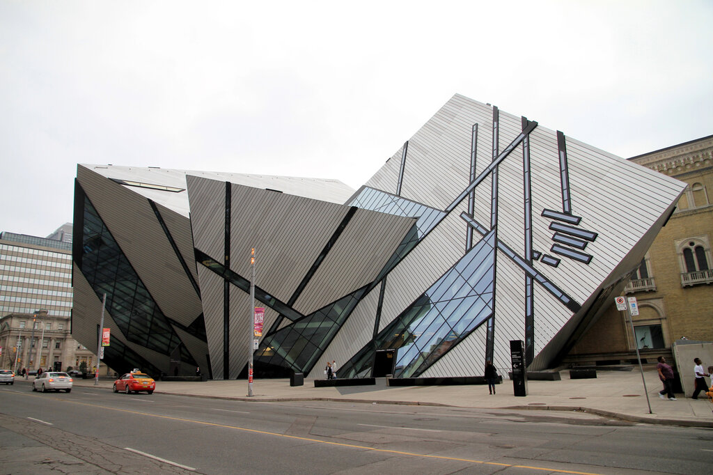 The sharp angular glass and aluminum exterior of the Royal Ontario Museum Michael Lee Chin Crystal rises above the street in downtown Toronto. The dramatic geometric structure contrasts with the historic stone building beside it.