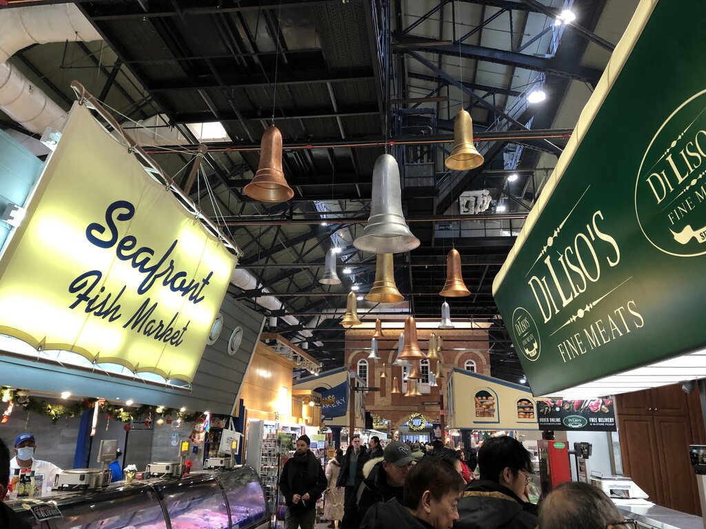 Busy indoor market aisle at St. Lawrence Market with shoppers walking between food stalls. Overhead signs read "Seafront Fish Market" and "Di Liso’s Fine Meats" hanging above the counters