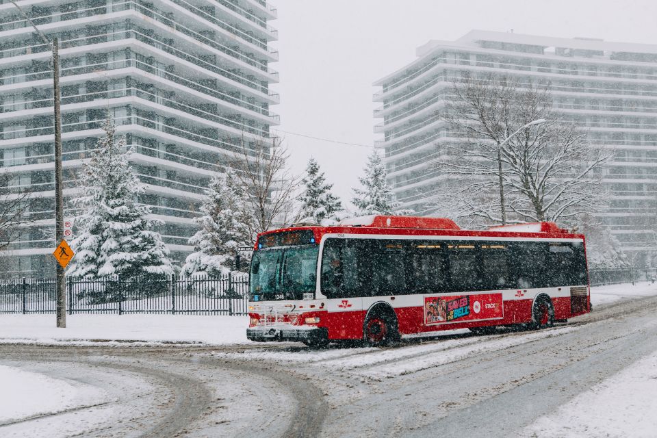 red city bus in toronto crossing a snow covered intersection with tall buildings behind the street.