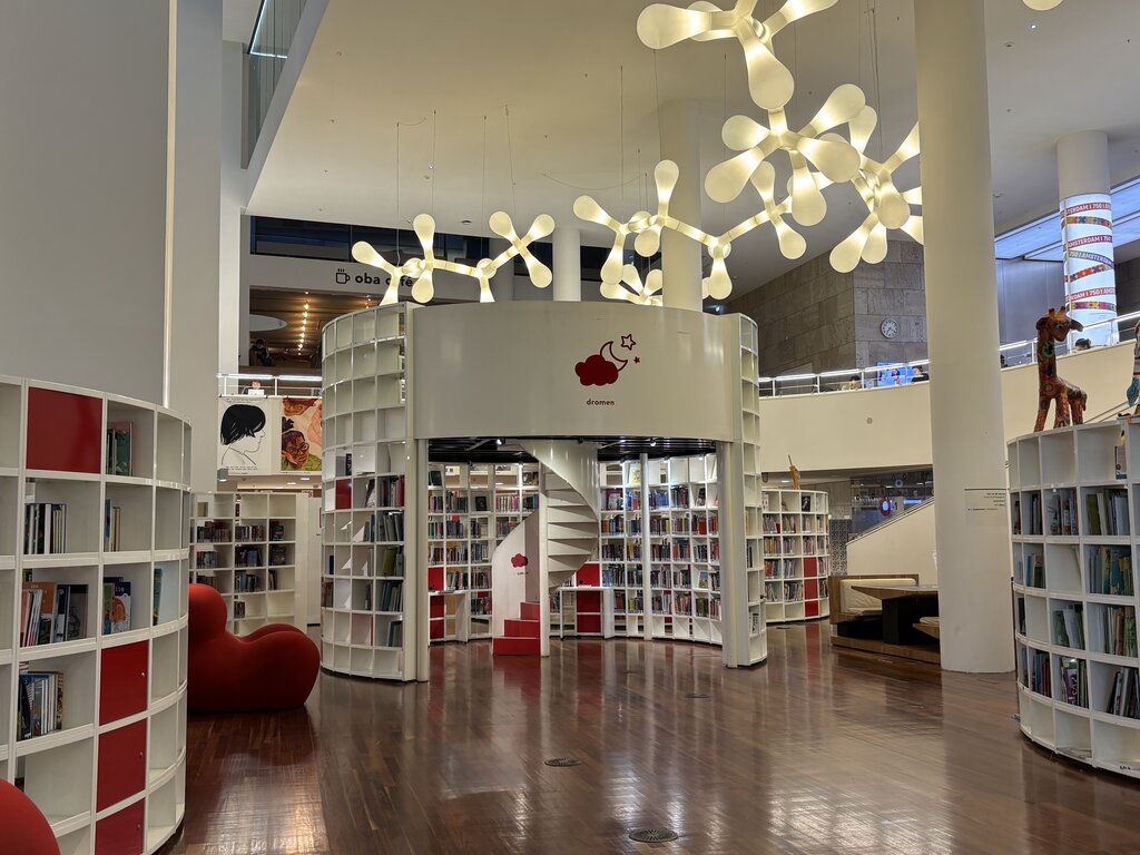 Modern library interior with curved white bookshelves filled with books a spiral staircase and large sculptural ceiling lights creating a bright open space, at the public library in Amsterdam
