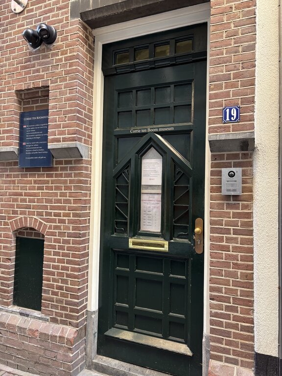 Dark green door marked "Corrie ten Boom museum" with the number "19" on a brick building entrance in Amsterdam.
