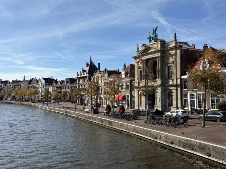 Canal side view in Amsterdam with historic buildings bicycles and trees lining the water and people walking along the street.