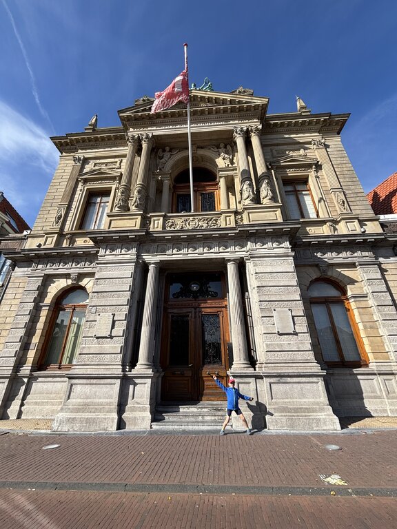 Ornate historic building with columns and decorative carvings with a child standing on the steps with arms raised in front of the entrance of the Teylers Museum in Haarlem, Netherlands