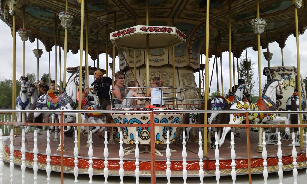 Children and adults ride a colourful carousel with painted horses while seated in the center section of the spinning ride at an outdoor fair.
