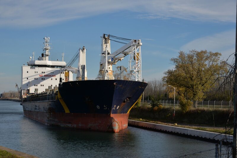 Large cargo ship docked along the Welland canal with cranes and equipment on deck and the text "NO SMOKING" visible on the side of the vessel.