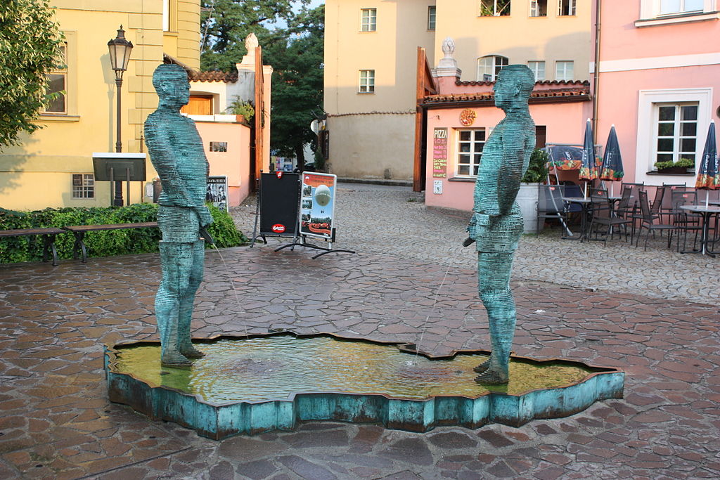 Two green bronze figures stand facing each other in a shallow fountain shaped like the map of the Czech Republic in a cobblestone square. The quirky sculpture is a popular stop for travellers looking for unusual things to see in Prague.