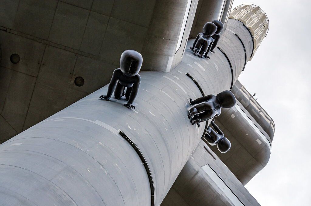 Black baby like sculptures climb a tall television tower viewed from below against a grey sky. The unusual installation creates a surreal scene and is one of the weird things to see in Prague.
