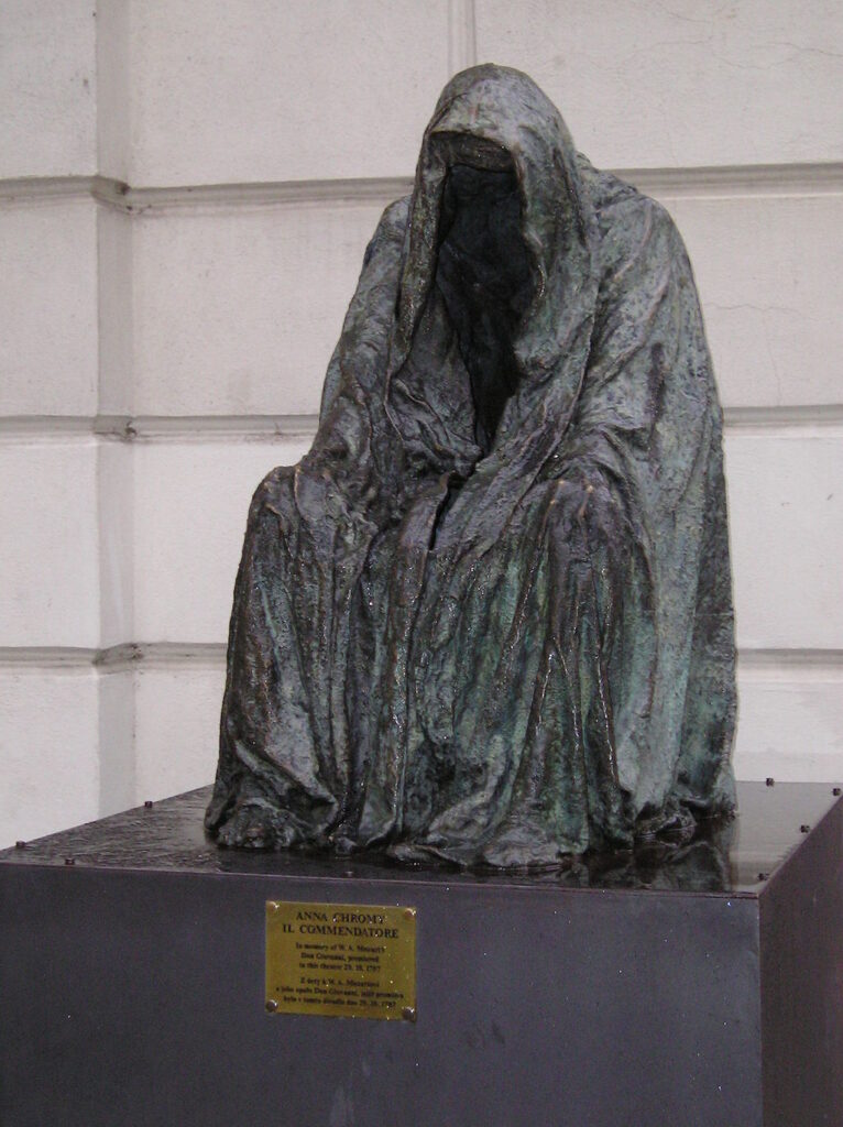 Dark hooded statue seated on a pedestal with an empty shadowed face hidden beneath heavy folds of fabric. The eerie sculpture creates a mysterious atmosphere and is among the more unusual sights in Prague.
