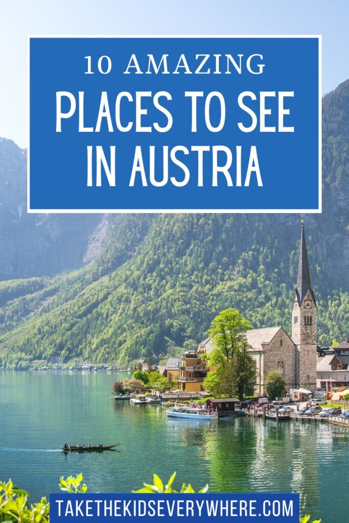 Hallstatt village beside a calm alpine lake with a stone church, boats, and forested mountains rising in the background. Text on the image reads "10 Amazing Places to See in Austria" and "TAKETHEKIDSEVERYWHERE.COM".