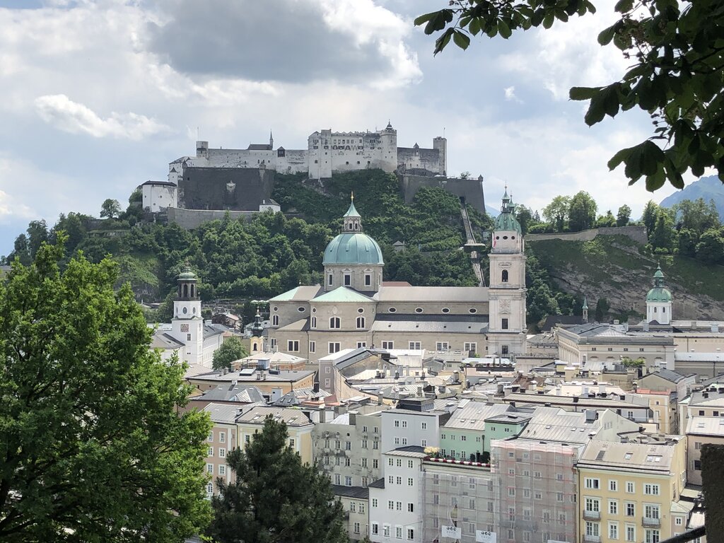 Elevated view over Salzburg with cathedral domes, pastel buildings, and Hohensalzburg Fortress overlooking the city from the hilltop.