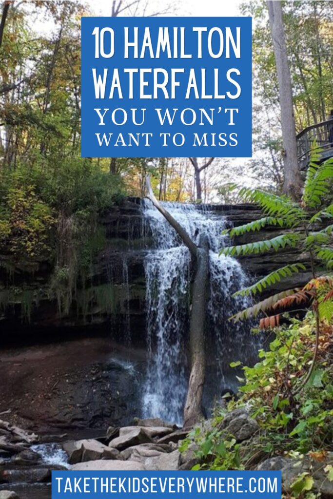 Waterfall cascading over layered rock in a wooded area with a fallen tree trunk leaning across the falls. Text reads "10 Hamilton Waterfalls You Won’t Want to Miss" and "TakeTheKidsEverywhere.com".