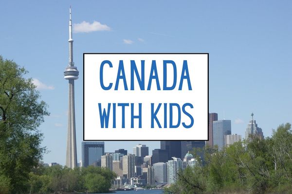 Toronto skyline and CN Tower seen across the water on a sunny day. A white graphic over the city reads "CANADA WITH KIDS".