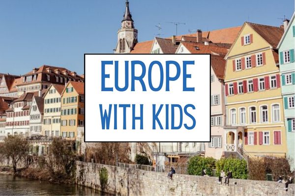 Colourful historic European buildings with red roofs line a river under a clear blue sky. A white graphic over the scene reads "EUROPE WITH KIDS".