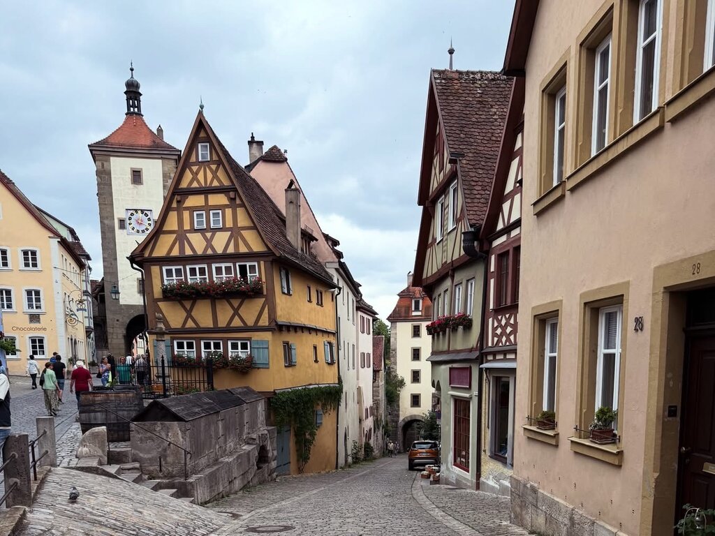 Cobblestone street winding between colourful half timbered houses in the historic European town of Rothenburg ob Tauer. A clock tower and flower filled window boxes add to the medieval streetscape.