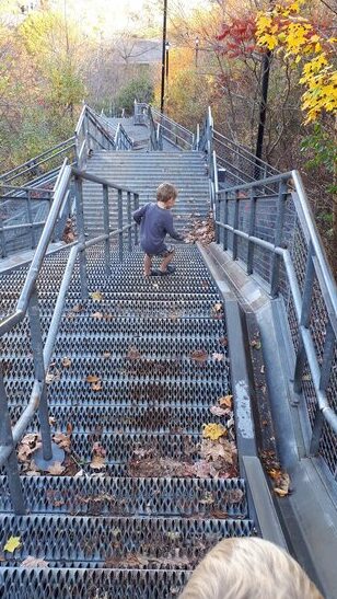 Child descends a long metal staircase through colourful autumn woodland in Hamilton Ontario. Bright yellow orange and red leaves surround the steep stairs.