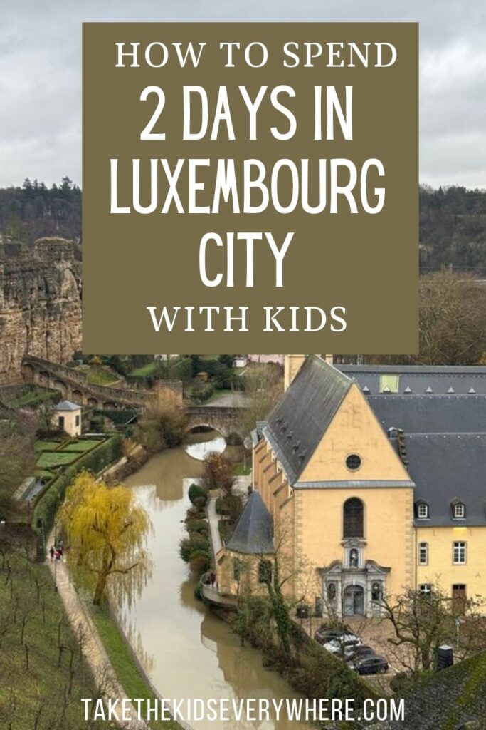 Luxembourg City viewed from above with a historic yellow building beside a narrow river and stone fortifications in the background. The graphic reads "HOW TO SPEND 2 DAYS IN LUXEMBOURG CITY WITH KIDS" and "TAKETHEKIDSEVERYWHERE.COM".