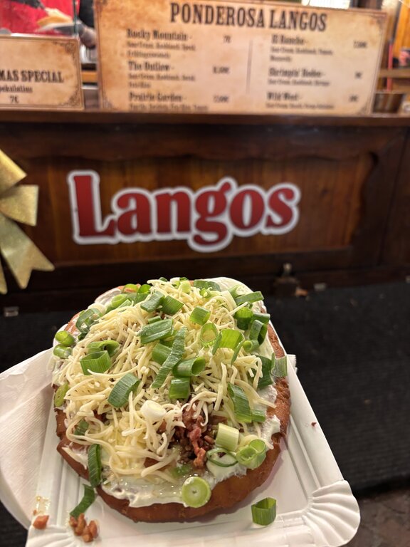 A freshly prepared savory flatbread piled with shredded cheese and green onions at a Luxembourg Christmas market. The food is held in front of the Langos market stall.